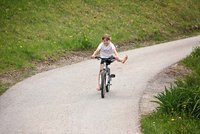 Ein Mädchen fährt auf einen Fahrrad auf einem Kiesweg. Sie macht Faxen auf dem Radn
