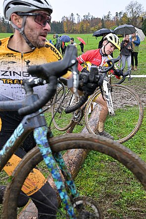 Radrennfahrer tragen ihre Velos über ein Hinderniss.