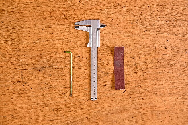 Inbusschlüssel, Messeschieber und Schleifpapier liegen auf einem Tisch
