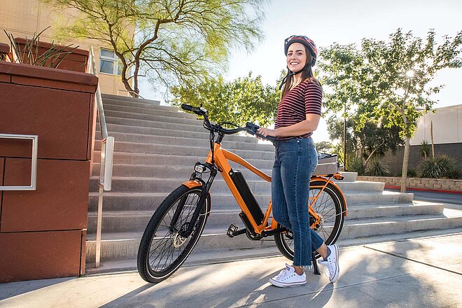 Jede dritte Person nutzte für Bike to Work ein E-Bike. Neuer Teilnehmerrekord bei Bike to Work. Eine junge Frau steht vor einem orange farbigen E-Bike.