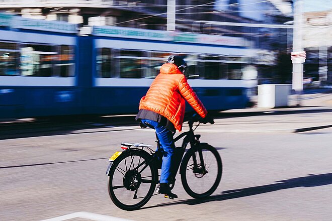 Avenir Suisse Studie Tempo ÖV Schweizer Städte. Eine Person mit oranger Jacke fährt in Zürich auf einem E-Bike.