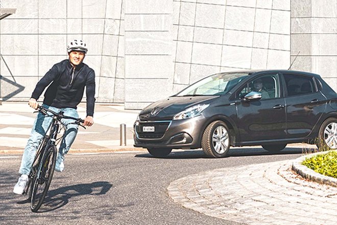 Ein Mann fährt mit dem Fahrrad durch einen Kreisverkehr, ihm folgt ein Auto.