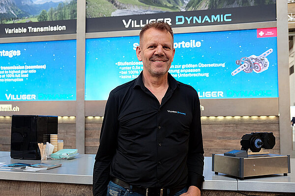 Villiger Dynamic E-Bike Antrieb. Ein Mann mit schwarzem Hemd steht an einer Messe.