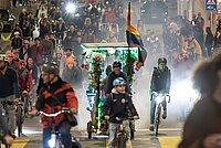 Velofahrende mit bunten Anhängern und bunten Rädern fahren auf einer Strasse.