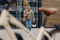 Bosch E-Bike Systems Battery Lock Schutz für E-Bike Akkus. Eine Frau mit Smartphone und Fahrradhelm läuft zu ihrem E-Bike.