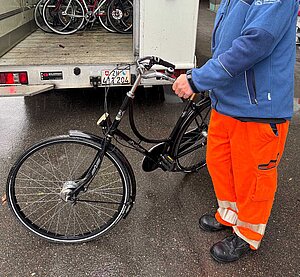 Ein Mann in Arbeitskleidung schiebt ein Fahrrad.