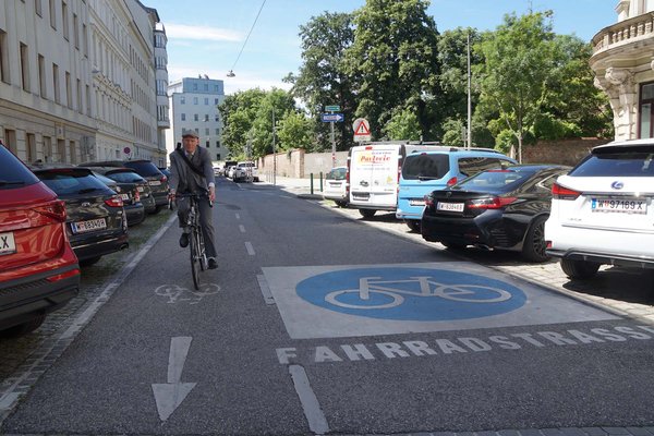 Ist Wien eine Velostadt? Ein Mann im grauen Anzug fährt mit dem Rad auf einer Strasse.