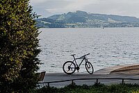 Richtplan Kanton Zug Alltags- Freizeitvelonetz. Ein Fahrrad steht an einem Seeufer. Auf der anderen Seiten des Sees ist ein Berg.