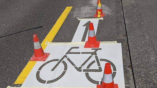 Auf einer Strasse werden Radstreifen und ein Velosignet aufgemalt.