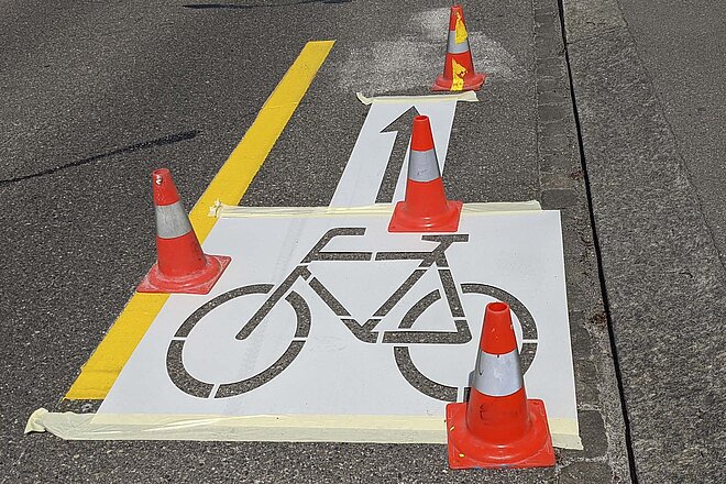 Auf einer Strasse werden Radstreifen und ein Velosignet aufgemalt.
