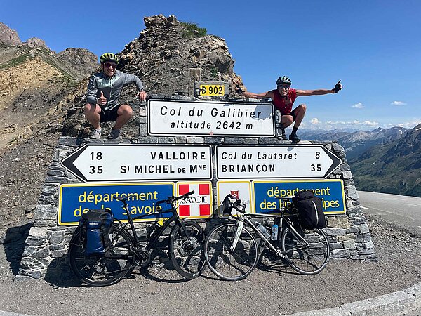 Zwei Männer mit Fahrradhelmen posieren neben Schildern.