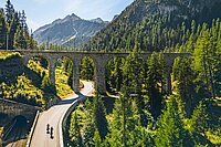 Strasse in den Alpen mit Viadukt im Hintergrund.