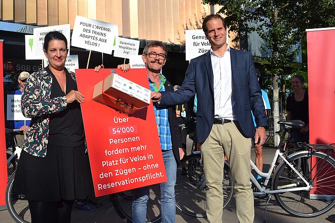 Delphine Klopfenstein (Pro Velo) und Ruedi Blumer (VCS) überreichen die Petition an Linus Looser, Leiter Produktion Personenverkehr SBB. (Foto: VCS) Drei Personen halten ein Transparent in die Höhe