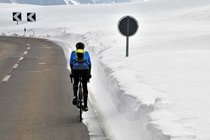 Ein Radfahrer fährt auf der Strasse, am Rand ist ein hoher Wall mit Schnee