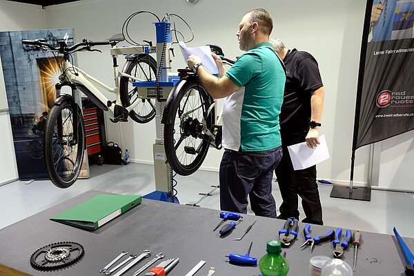 Personen arbeiten in einer Fahrradwerkstatt an einem Fahrrad. 