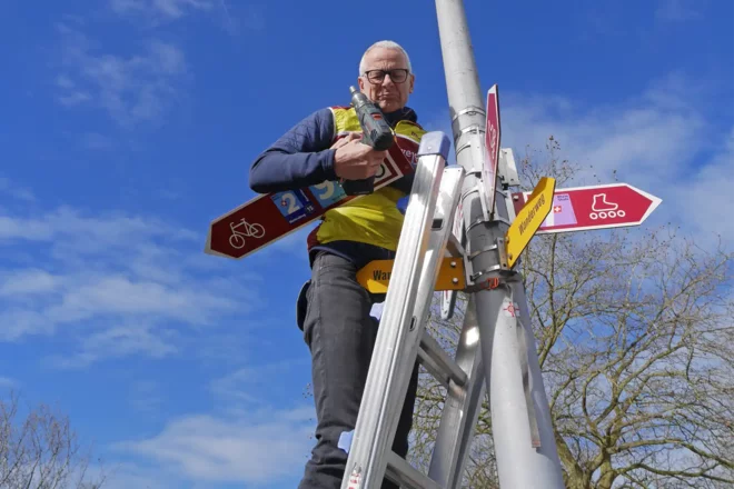 Ein Mann steht auf einer Leiter und montiert Schilder des Veloland Schweiz.