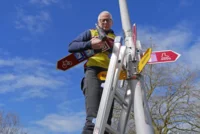 Ein Mann steht auf einer Leiter und montiert Schilder des Veloland Schweiz.