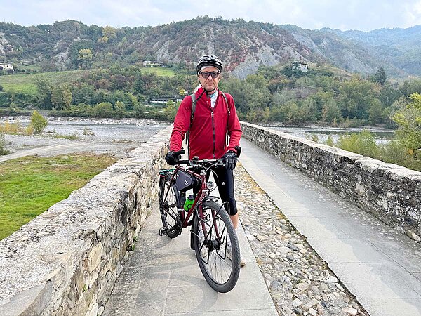 Ein Radfahrer mit roter Jacke steht auf einer Brücke.