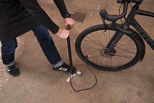 Eine Person pumpt mit einer Standpumpe einen Veloreifen