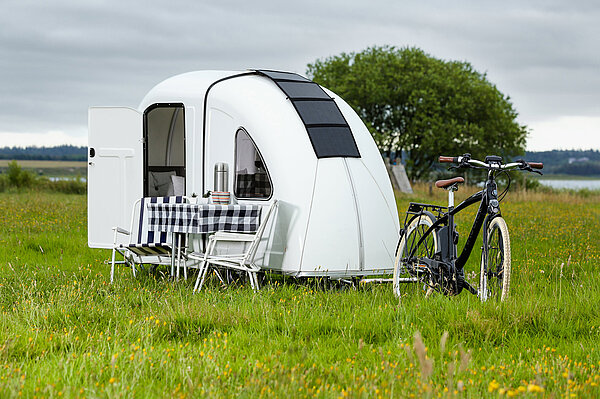 Camperanhänger mit Velo auf einer Wiese.