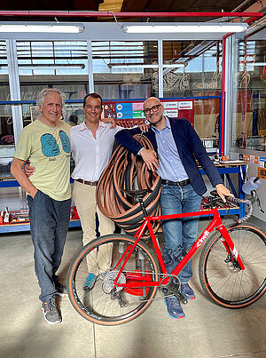 Drei Männer stehen hinter einem roten Gravel Fahrrad