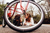 Kinder und Jugendliche unter 16 Jahren müssen in der Schweiz weiterhin keinen Velohelm tragen. Zwei junge Frauen liegen auf der Strasse hinter einem Velo.