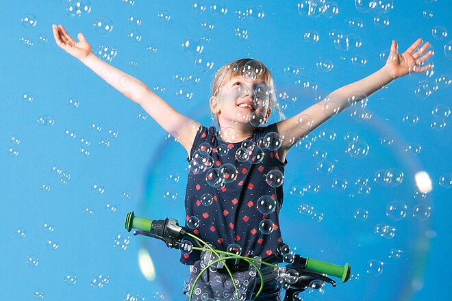 Spiele, die Kinder das Radfahren lehren. Ein Mädchen fängt Seifenblasen auf dem Fahrrad.