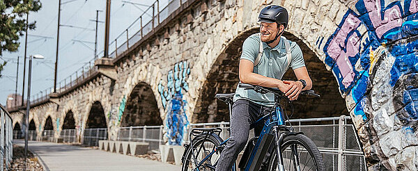 Ein Mann steht mit seinem E-Bike neben einer Brücke