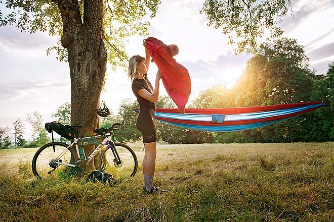 Tipps draussen schlafen auf der Velotour. Eine Frau in Fahrradbekleidung steht neben einer Hängematte.