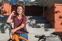 Eine Frau steht hinter einem orange farbenem Velo. 