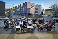 Alber Koechlin Stiftung AKS clever unterwegs. Eine Gruppe von Personen steht mit Cargobikes auf einem Platz.
