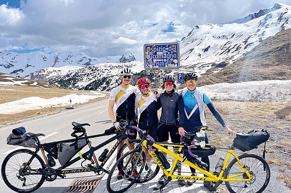 Fahrrad Tandem Reise Italien. Personen stehen vor dem Schild eines Strassenpasses.