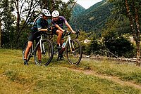 Zwei Frauen auf Gravelbikes schauen auf dem Smarphone eine Strecke nach. 