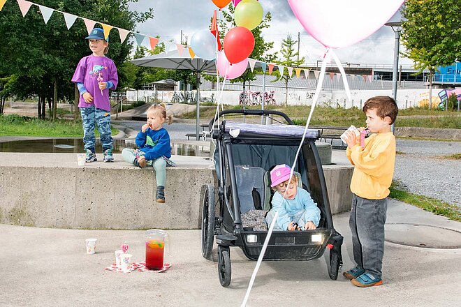Kinder sitzen in einem Kindernahänger für Fahrräder.