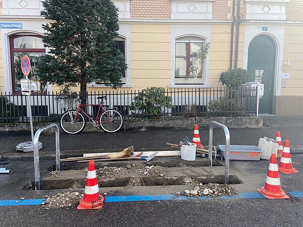 Baustelle mit Pilonen vor gelbem Haus. Parkplatz wird zum Veloabstellplätz umgebaut.