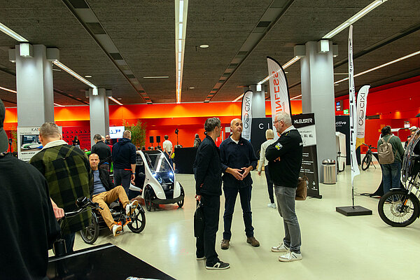 Personen stehen in einer Halle zwischen Messeständen.