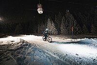 Ein Biker fährt mit dem Bike in der Nacht auf einer beleuchteten Skipiste. 