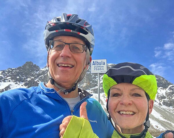 Zwei Personen mit Fahrradhelm posieren für ein Foto auf einem Alpenpass.