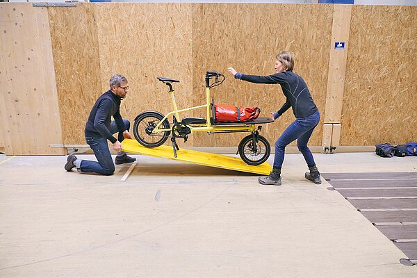 Zwei Personen stellen ein gelbes Fahrrad auf ein gelbes Brett.
