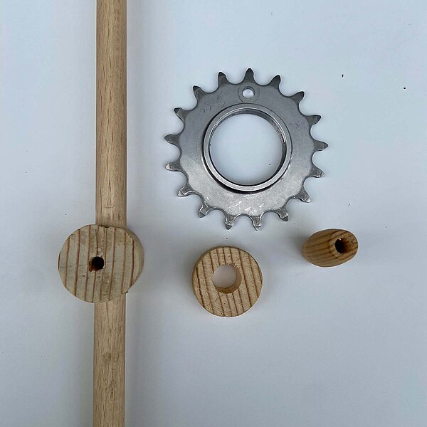 Bohren: Fixie-Ritzel Ø 5 mm*. Holzperle mittig Ø 6 mm. Rundholz quer mittig, Scheiblette mittig Ø 12 mm. Stab in Rundholz platzieren. Mittig Ø 6 mm durch Rundholz samt Stab bohren. DIY Velofisch