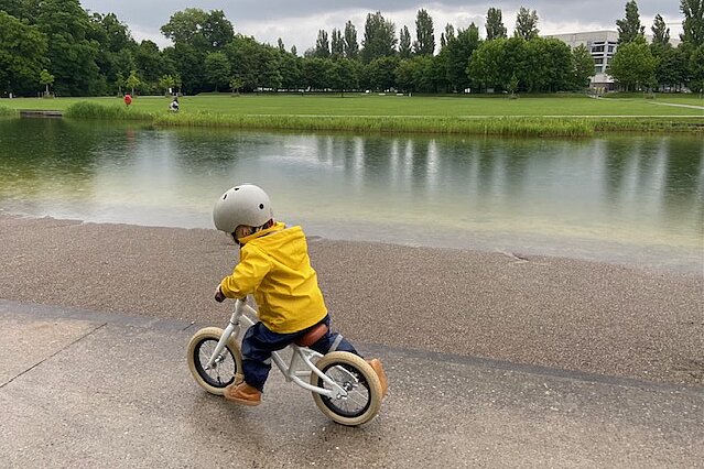 Ein Kind mit gelber Jacke fährt auf einem Laufrad.