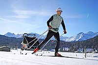Ein Mann fährt auf Langlaufski und zieht einen Schlitten hinter sich her.