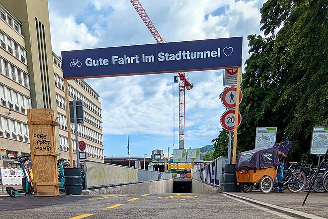 Tunneleinfahrt mit einem darüber gespannten Transparent, das gute Fahrt wünscht.