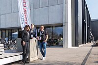 Zwei Männer und eine Frau stehen vor einem grauen Haus