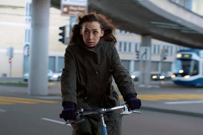 Eine Frau fährt im Wintermantel mit dem Velo durch die Stadt