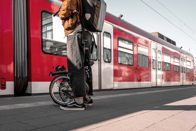 Die Deutsche Bahn und der Faltrad-Hersteller Brompton haben im Raum Stuttgart ein Pilotprojekt gestartet. Eine Person steht mit dem Faltvelo auf dem Bahnsteig.