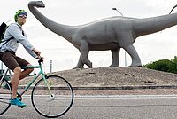 Ein Mann fährt auf einem Velo durch einen Kreisel, auf dem Kreisel steht ein Dinosaurier