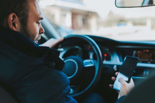 Ford will Autolenker per App vor Velos und Personen zu Fuss warnen. Ein Autofahrer blickt auf sein Smartphone.