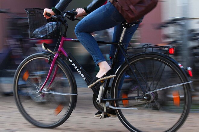 Eine Frau fährt auf einem Citybike, im Lenkerkorb hat sie eine Flasche Wasser.