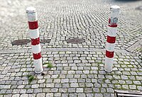 Zwei rotweisse Verkehrspoller zwischen Pflastersteinen